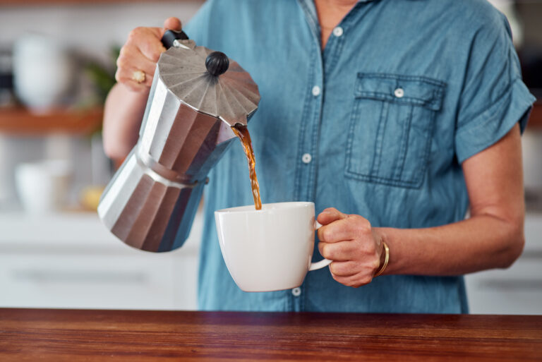 Woman in kitchen pouring coffee into a mug using a moka pot